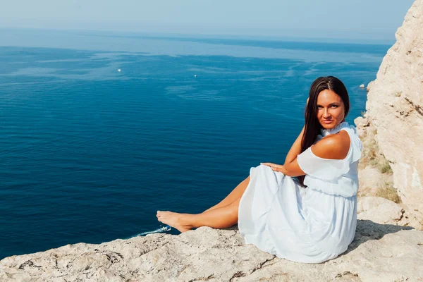 Beautiful tanned woman in blue dress on top of a cliff by the sea — Stock Photo, Image