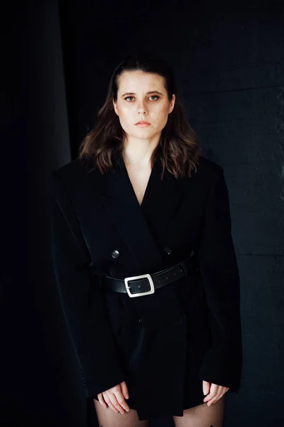 Portret van een mooie modieuze vrouw in een zwart jasje tegen een zwarte muur — Stockfoto