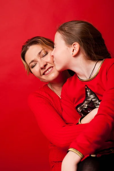 Mamá e hija cariñosamente acurrucadas sobre un fondo rojo — Foto de Stock