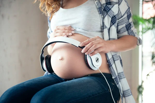 Těhotná žena drží sluchátka na břiše. — Stock fotografie