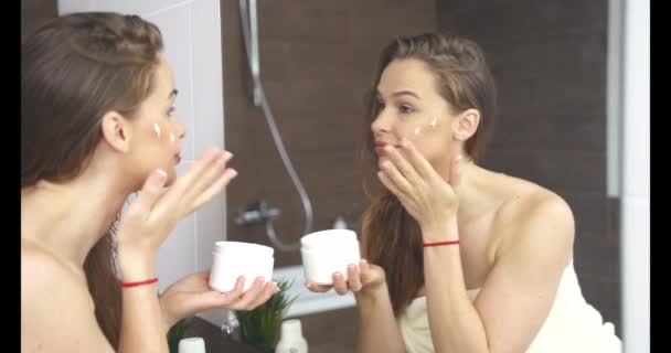 Vrouw aanbrengen crème op de huid, terwijl gezicht make-up op spiegel in de badkamer. — Stockvideo