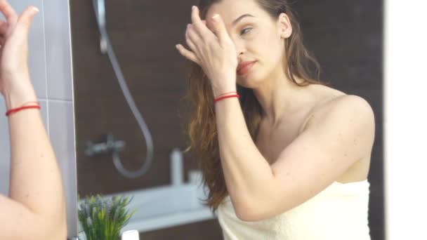 妇女在浴室镜面化妆时在皮肤上涂奶油. — 图库视频影像