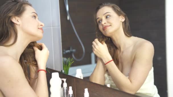 Banyodaki 4K görüntüde aynaya bakan güzel genç bir kadın. — Stok video