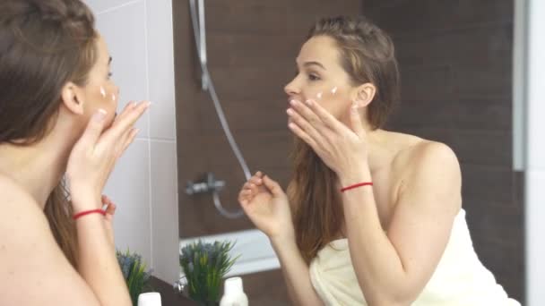 Woman applying cream to skin while face makeup at mirror in bathroom. — Stock Video