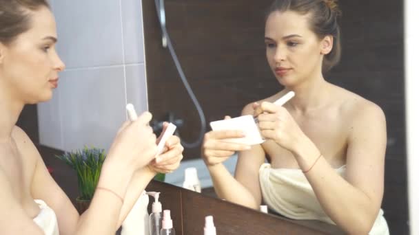 Mooie vrouw, doet make-up voor spiegel in de badkamer — Stockvideo