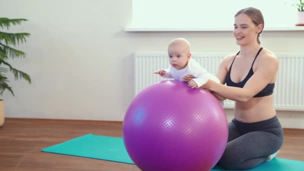 Wesoły matka bawi się dziecko, co dziecko fitness ćwiczenia na dużą piłkę — Wideo stockowe