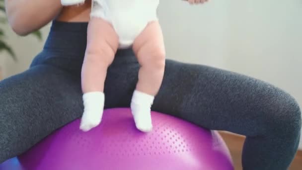 Alegre madre jugando con el bebé, haciendo ejercicios de fitness del bebé en la bola grande — Vídeo de stock