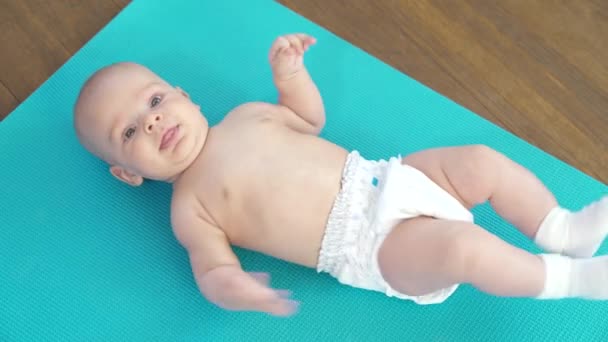 Neonato bambino in un pannolino senza vestiti si trova su un tappeto fitness — Video Stock