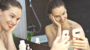 Gülümseyen Kadın, tuvaletteki aynada cep telefonundan selfie çekiyor..