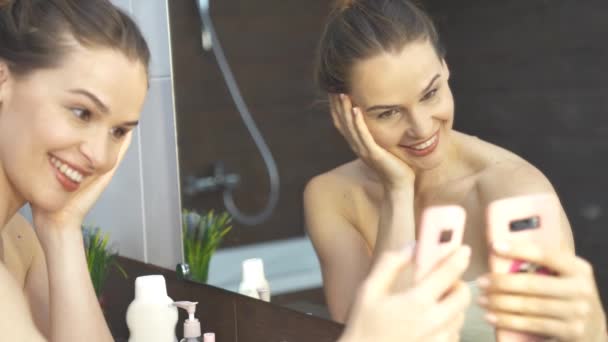 Mujer sonriente tomando foto autofoto móvil en el teléfono en el espejo del baño . — Vídeos de Stock