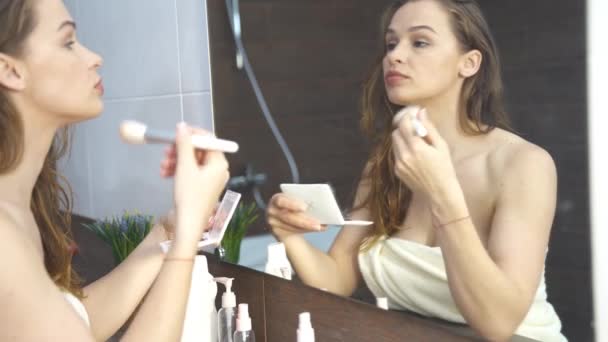 Όμορφη γυναίκα να κάνει μακιγιάζ μπροστά από τον καθρέφτη στο μπάνιο — Αρχείο Βίντεο