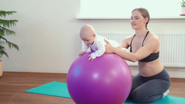 Fröhliche Mutter spielt mit Säugling, macht Baby-Fitnessübungen auf großem Ball — Stockvideo