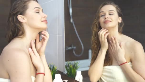 Woman applying cream to skin while face makeup at mirror in bathroom — Stock Video