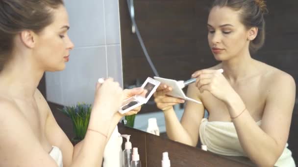 Vacker kvinna gör makeup framför spegeln i badrummet — Stockvideo