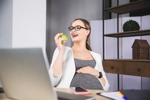 Joven embarazada sosteniendo manzana en la oficina — Foto de Stock