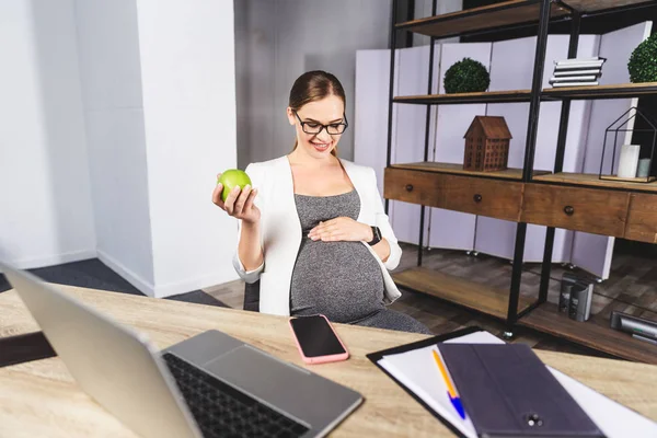 Joven embarazada sosteniendo manzana en la oficina — Foto de Stock
