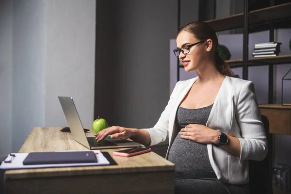 Mujer embarazada joven de negocios utilizando un ordenador portátil en la oficina — Foto de Stock