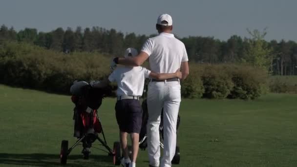 Счастливый мужчина с сыном гуляют по идеальному полю для гольфа в летний день — стоковое видео