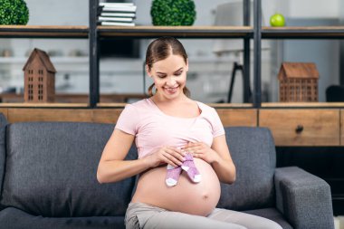 Evdeki kanepede güzel bebek çoraplarıyla güzel hamile bir kadın.