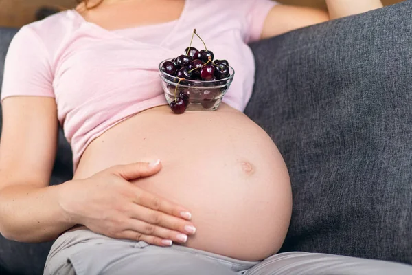 Den gravida kvinnan håller en tallrik med körsbär. Stockfoto