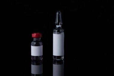 Kırmızı kapaklı küçük bir şişe ve siyah arka planda çeşitli ilaçlardan oluşan tıbbi ampul. Antibiyotikler, aşılar veya diğer enjekte edilebilir ilaçlar