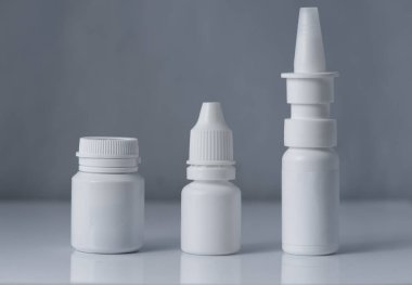 Beyaz, gri arka planda 3 beyaz plastik tıbbi kap.