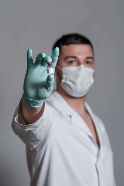 白い医療用のガウンを着た美しい医者が顔に薬や注射器の瓶を手袋で手に持っている — ストック写真