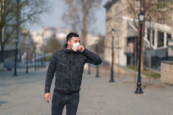 Virus covid-19. A man in a medical mask sneezes and coughs on a street in a city in Europe. Pandemic mask virus protection.