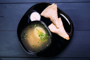 Siyah zemin üzerinde krep ve ekşi krema olan siyah bir tabakta yumurtalı taze balık çorbası. Mavi tahta arkaplan