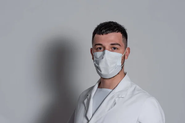 白地に仮面をつけた白地のコートを着たブルネットの医者の肖像画 — ストック写真