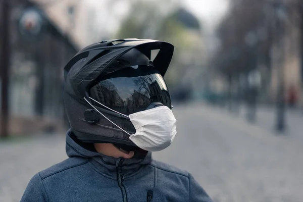 portrait of a man in a helmet. on a motorcycle helmet a white medical mask. photo on the street against the background of houses. coronavirus, disease, infection, quarantine, covid-19