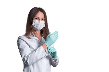 Genç bayan hemşire cerrahi ya da tıbbi maske takıyor. Beyaz bir bornoz ve beyaz arka planda izole edilmiş eldivenler giyen bir doktor. covid 19, koronavirüs, karantina