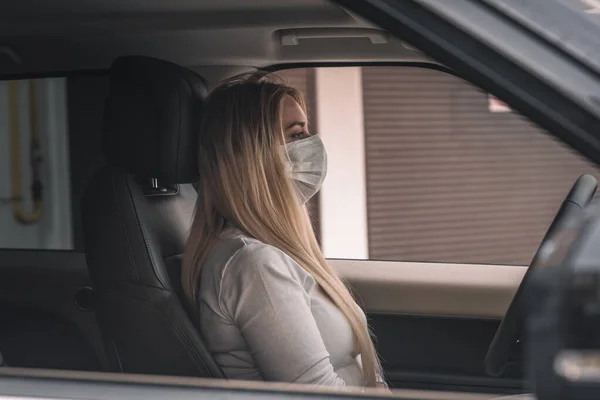 Beautiful young girl in a mask sitting in a car, protective mask against coronavirus, driver on a city street during a coronavirus outbreak, covid-19