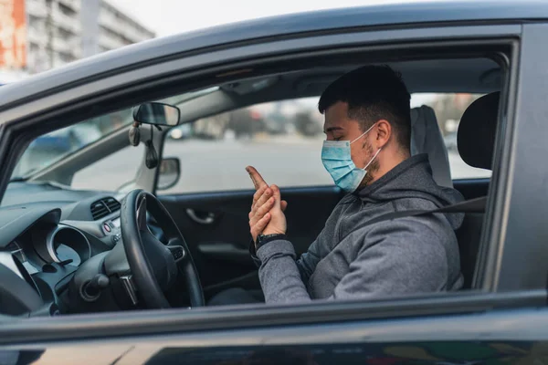 一个男人坐在车里用防腐液洗手 汽车保健概念 面具在脸上是白色的 Coronavirus Disease Infection Quarantine Covid 免版税图库照片