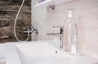 Banyoda beyaz lavabo, el dezenfeksiyonu, halı 19, dezenfektan, sabun ve musluk.