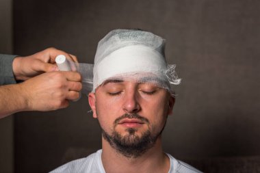 Sakallı adamın sargılı kafası. Eller bir insanın kafasına gazlı bez sarıyorlar. Evde ilk yardım. Coronavirus, covide 19, karantina