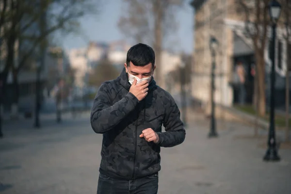 Virus covid-19. A man in a medical mask sneezes and coughs on a street in a city in Europe. Pandemic mask virus protection.