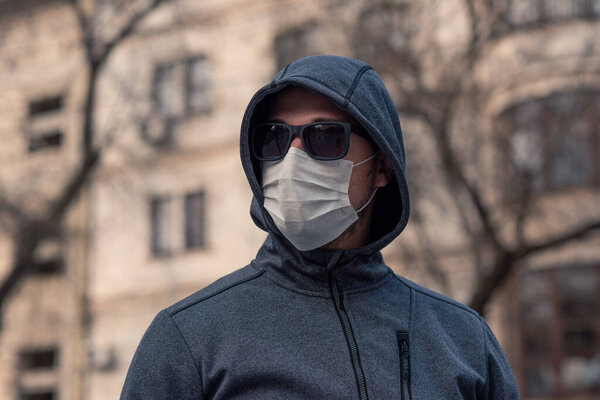 portrait of a brunette man in a surgical dressing and black glasses against the backdrop of a modern building, coronavirus, disease, infection, quarantine, medical mask