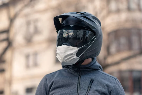 portrait of a man in a helmet. on a motorcycle helmet a white medical mask. photo on the street against the background of houses. coronavirus, disease, infection, quarantine, covid-19