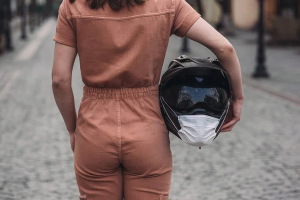 Девушка Стоит Комбинезоне Держит Руке Мотоциклетный Шлем Медицинской Маской Фото — стоковое фото