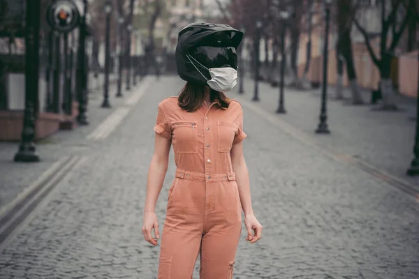 slender girl in overalls. A woman is standing in a motorcycle helmet with a medical mask. Photo without a face. Against the background of the street and road. coronavirus, disease, infection, quarantine, covid-1