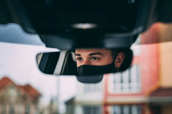 黒い医療マスクの男 ハンサムなブルネットが車を運転してる 車の鏡の中の写真 コロナウイルス 感染症 医療マスク Covid ロイヤリティフリーのストック画像