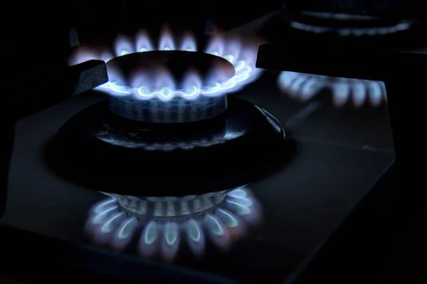 Burning gas stove hob blue flames close up in the dark on a blac — Stock Photo, Image