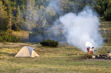 Bir çadır, kamp ateşi zeka duman ve turist su uzun yürüyüşe çıkan kimse ile göster