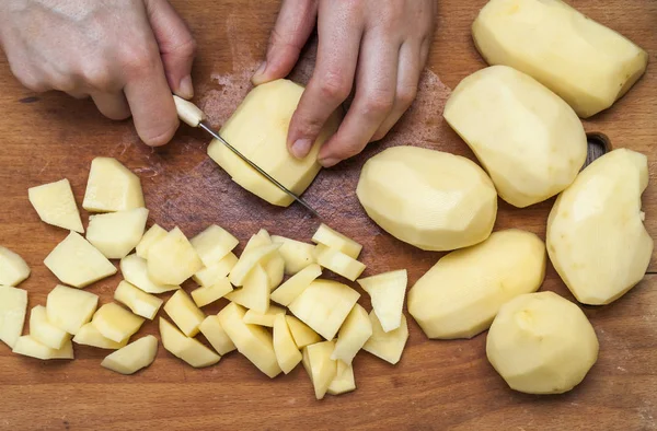 A mão da mulher com uma faca cortando batatas em madeira boa — Fotografia de Stock