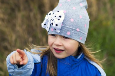 Bulanık arka planda poz veren sevimli küçük bir kız ve kameraya gülümsüyor. Kışlık paltosu ve şapkası vardı. Sonbaharda açık havada güzel bir genç kız.