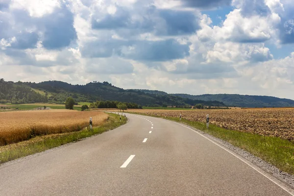 Асфальтированная сельская дорога в Германии через зеленое поле и облака на голубом небе в летний день . — стоковое фото