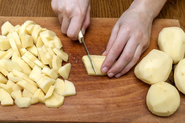 Женская рука с ножом, режущим картошку на деревянном боа — стоковое фото