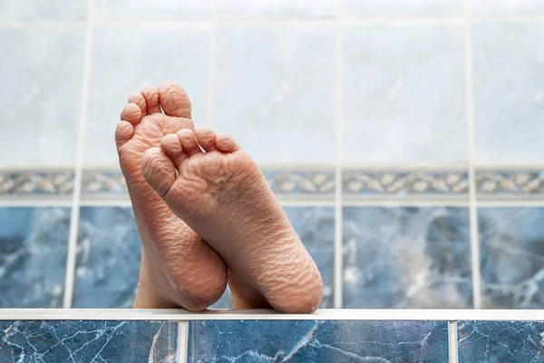 Skrynkliga nakna fötter kommer ut ur ett badkar. Ung person getti — Stockfoto