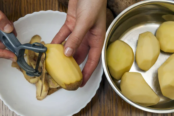 Деталь женских рук, очищающих свежий желтый картофель с кухней п — стоковое фото